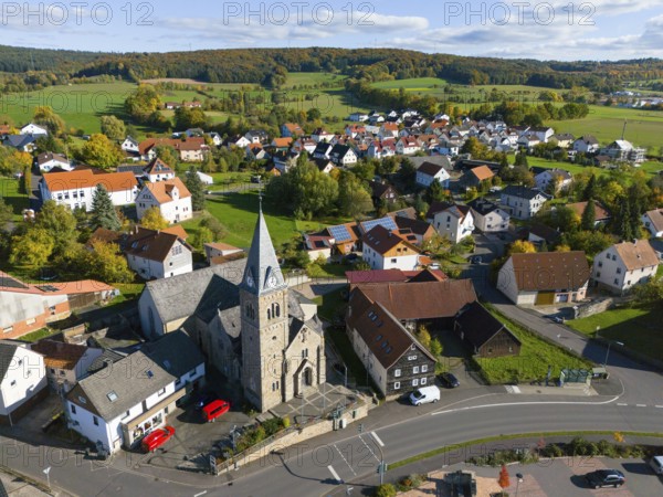 A village with church surrounded by hills and green meadows in autumn, aerial view, Niederkalbach, Kalbach municipality, Fulda district, Hessian Rhön nature park Park, Hesse, Germany