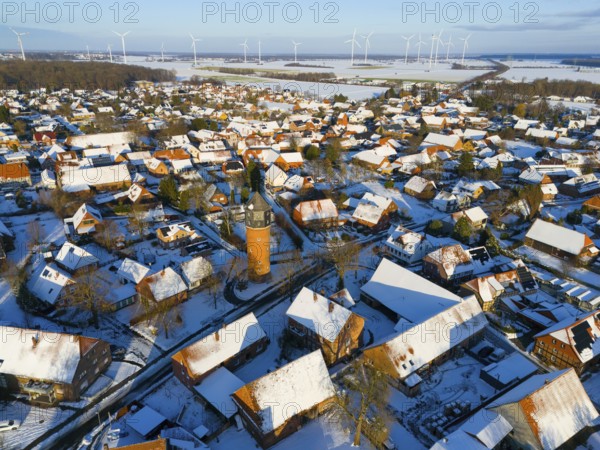 Snowy village with a central water tower surrounded by wind turbines and snow-covered houses under a clear sky, aerial view, water tower, museum, Groß Lafferde, municipality of Ilsede, district of Peine, Lower Saxony, Germany