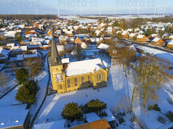 Snowy church in a village with a rural atmosphere, surrounded by wind turbines in a quiet winter landscape, aerial view, Bernwardskirche, Groß Lafferde, municipality of Ilsede, district of Peine, Lower Saxony, Germany