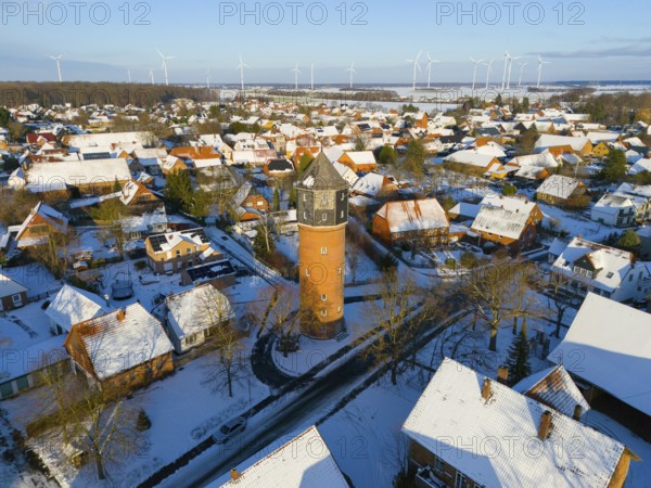 Village with a water tower in the midst of a wintry landscape, surrounded by snow-covered houses and wind turbines, aerial view, water tower, museum, Groß Lafferde, municipality of Ilsede, district of Peine, Lower Saxony, Germany