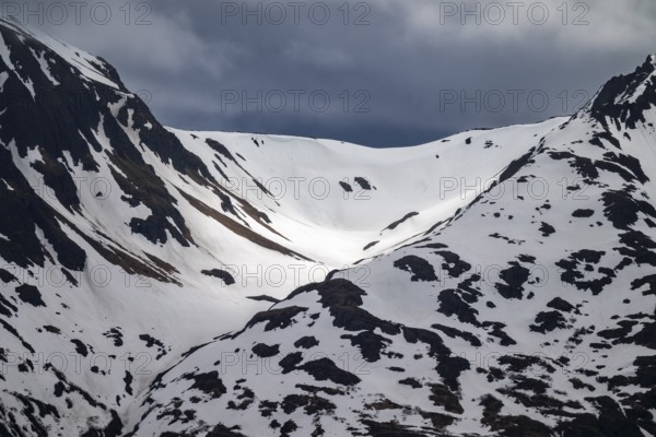 Mountain ridge with snow in spring against dark dramatic cloudy sky, Alaska, USA