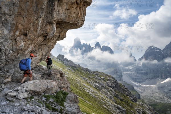 Two mountaineers on a path in front of a picturesque mountain landscape with rocky peaks, Via Ferrata SOSAT via ferrata, Cima Tosa summit in the back, Brenta Mountains, Trentino, Italy