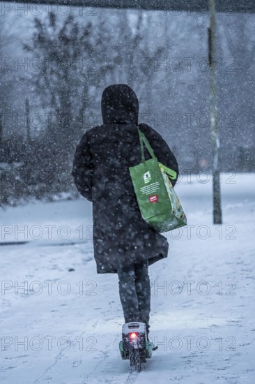 Winter weather, blowing snow, woman with e-scooter on snowy road, North Rhine-Westphalia, Germany