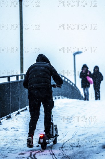 Winter weather, blowing snow, man with e-scooter trying to make his way uphill on a snowy sidewalk, on a footbridge, North Rhine-Westphalia, Germany