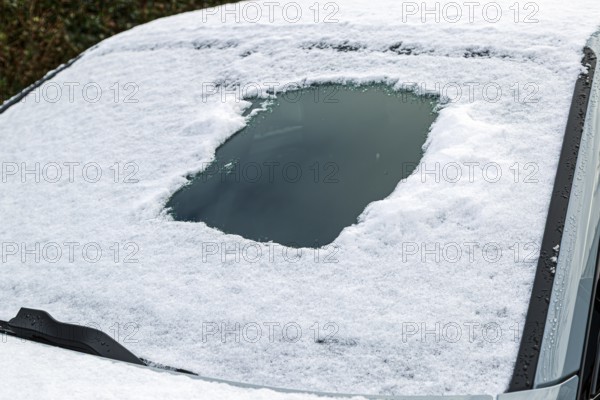 Snow-covered car window with scratched peephole area, typical winter scene