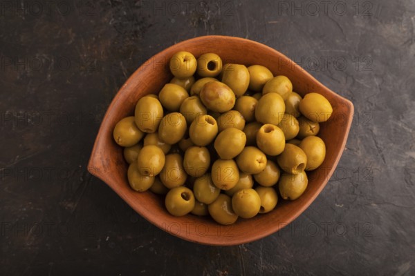 Fresh green olives in ceramic clay bowl on black concrete background. Top view, flat lay, close up