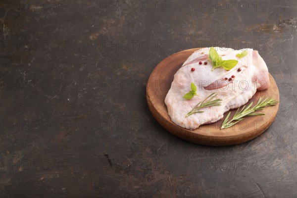 Raw Turkey Thigh with spices and rosemary on cutting board on black concrete background. side view, copy space