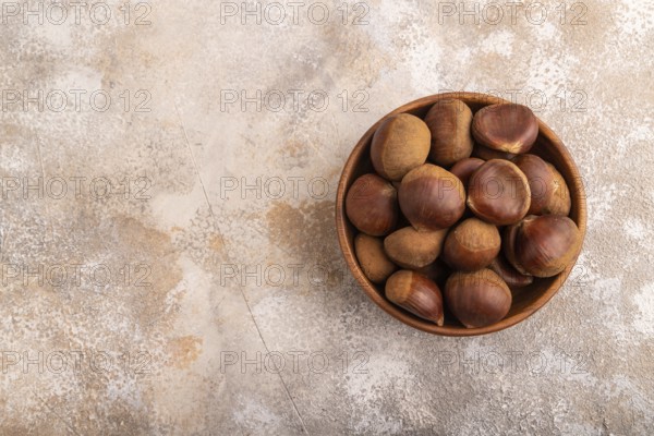 Wooden bowl with raw edible ?hestnuts on brown concrete background, top view, flat lay, copy space, minimalism