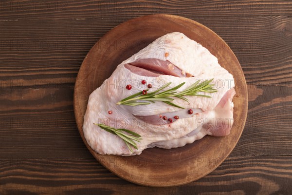 Raw Turkey Thigh with spices and rosemary on cutting board on brown wooden background. top view, flat lay, close up