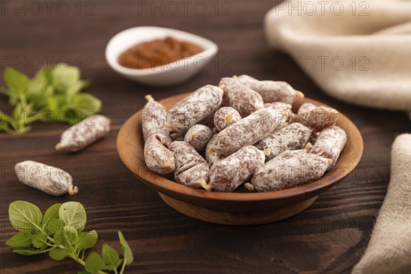 Small smoked Chicken sausages in wooden bowl on brown wooden background and linen textile. side view, close up, selective focus