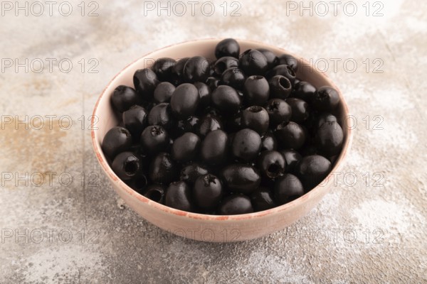 Fresh black olives in ceramic bowl on brown concrete background. side view, close up