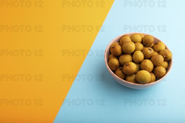 Ripe Longan in ceramic bowl on blue and orange pastel paper background, side view, copy space, minimalism