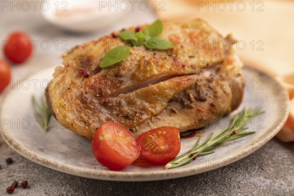 Fried Turkey Thigh with spices and rosemary on plate on brown concrete background and orange linen textile. side view, close up, selective focus