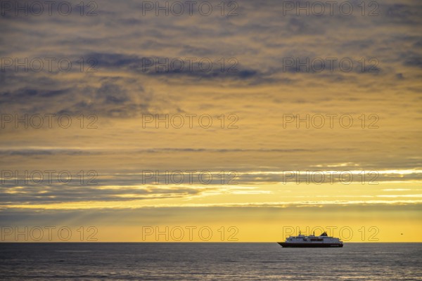 A Hurtigrute ship on the wide Barents Sea at sunset midnight sun, yellowish clouds and calm seas, Berlevåg, Finnmark, Norway