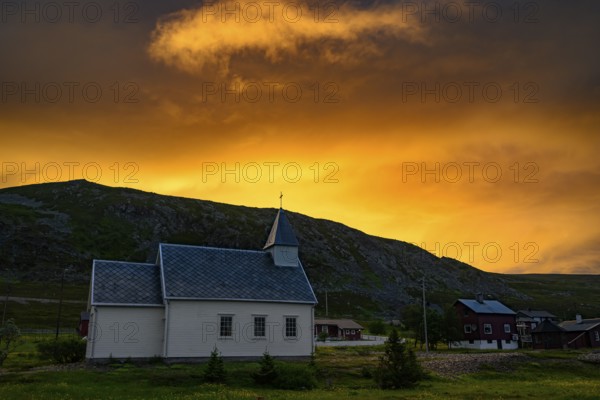 Nordford chapel on Ytre Syltefjord under a dramatic evening sky surrounded by cloudy sky, small church with rainbow in the sky, dramatic cloud formationsNordfjord, Båtsfjord, Finnmark, Norway