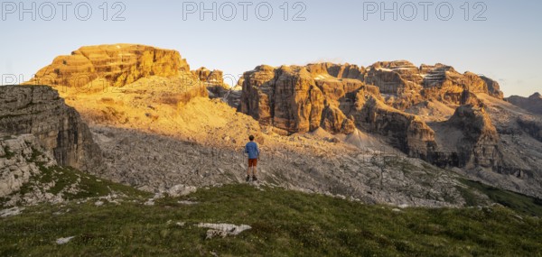 Mountaineer enjoying the view of rocky mountain peaks of the Brenta Mountains at sunset, Alpenglühen, mountain landscape on the Grosté Plateau, Brenta, Parco Naturale Brenta-Adamello, Trentino, Italy