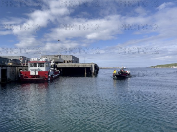 Port of the town of Vardö with the harbour master's ship and the incoming a running rigid dinghy speedboat that drives tourists to the bird island of Hornoy, Vardø, Finnmark, Norway
