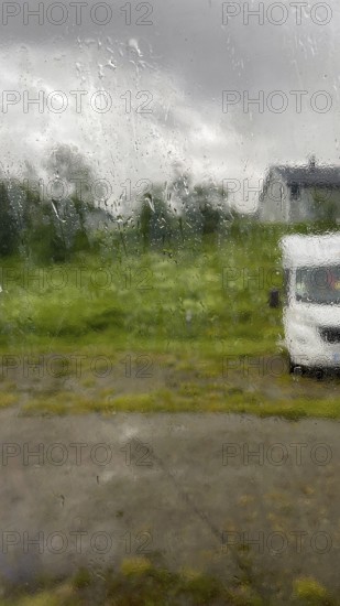 Looking through the rainy glass of a window, rain dripping along the window, cloudy sky, motorhome and green grass, Finnmark, Norway