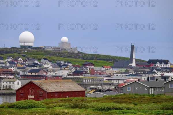 Vardø, Finnmark, Norway, city view with radar towers and a red warehouse in the foreground, under a cloudy sky, coastal town under grey sky with radar station in the background