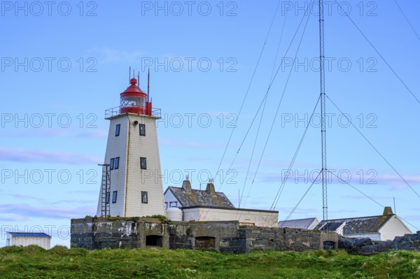 White lighthouse with red tip and antennas on the bird island of Hornoya, surrounded by grassy hills under clear skies, Vardø, Finnmark, Norway