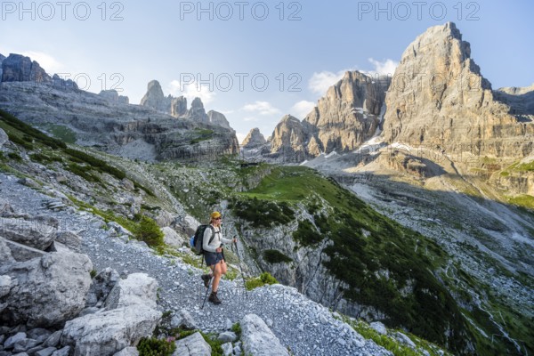 Female mountaineer hiking on a hiking trail in front of picturesque mountain scenery in the morning, Rifugio Ai Brentei mountain hut and Cima Tosa rock summit, Brenta, Trentino, Italy