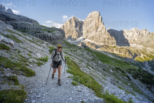 Female mountaineer in front of picturesque mountain landscape in the morning, Rifugio Ai Brentei mountain hut and Cima Tosa rock peak, Brenta, Trentino, Italy