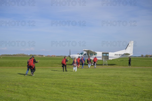 People with parachute equipment in front of a small plane on a green field, taking off for a tandem jump at Paracentrum Texel, North Holland, the Netherlands