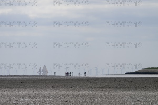 People and sailing ships in the Wadden Sea at low tide with wind turbines on the horizon, people on the beach with boats and wind turbines in the distance, Oosterend, Noord-Holland, the Netherlands