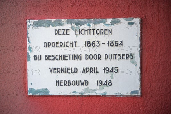 Memorial plaque on a red wall with text about the lighthouse de Cocksdorp and historical events of construction and destruction, Texel island, North Holland, the Netherlands