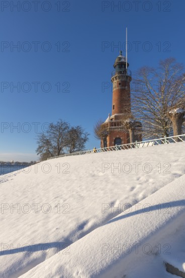 Holtenau lighthouse at the entrance of the Kiel Canal in winter, west bank of the Kiel Fjord, shipping, brick building from 1895, round tower, orientation, sea sign, beacon, ground floor with wedding room, trees, hills, snow, blue sky, Baltic Sea, Kiel, Germany