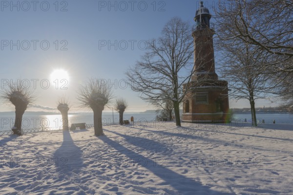 Holtenau lighthouse at the entrance of the Kiel Canal in winter, west bank of the Kiel Fjord, shipping, brick building from 1895, round tower, orientation, sea sign, beacon, ground floor with wedding room, trees, snow, blue sky, back light, sun, Baltic Sea, Kiel, Germany