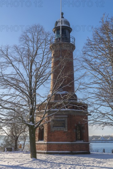 Holtenau lighthouse at the entrance of the Kiel Canal in winter, west bank of the Kiel Fjord, shipping, brick building from 1895, round tower, orientation, sea sign, beacon, ground floor with wedding room, trees, snow, blue sky, Baltic Sea, Kiel, Germany