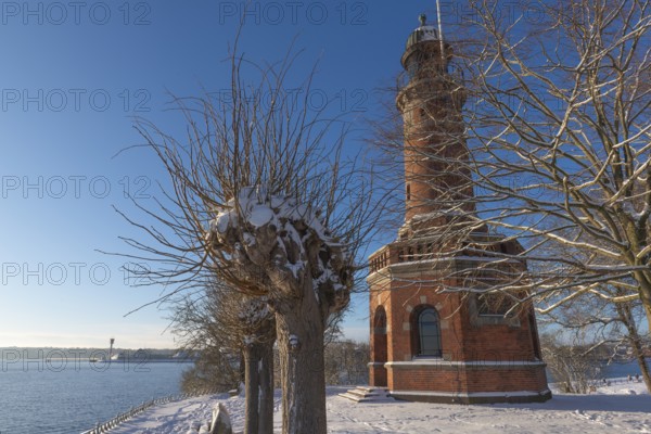 Holtenau lighthouse at the entrance of the Kiel Canal in winter, west bank of the Kiel Fjord, shipping, brick building from 1895, round tower, orientation, sea sign, beacon, ground floor with wedding room, trees, snow, blue sky, Baltic Sea, Kiel, Germany
