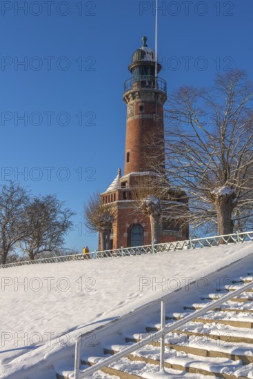 Holtenau lighthouse at the entrance of the Kiel Canal in winter, west bank of the Kiel Fjord, shipping, brick building from 1895, round tower, orientation, sea sign, beacon, ground floor with wedding room, trees, hills, steps, snow, blue sky, Baltic Sea, Kiel, Germany