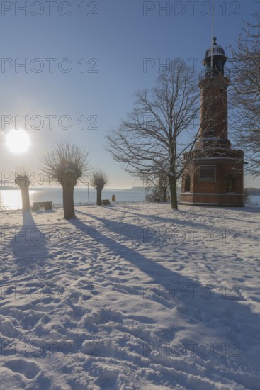 Holtenau lighthouse at the entrance of the Kiel Canal in winter, west bank of the Kiel Fjord, shipping, brick building from 1895, round tower, orientation, sea sign, beacon, ground floor with wedding room, trees, snow, blue sky, back light, sun, Baltic Sea, Kiel, Germany