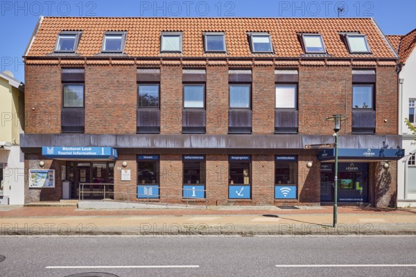 Tourist information, library leak, public library, commercial building, brick building, façade with windows, entrance with door and ramp, stainless steel railing, shop window, lantern, blue sky, cloudless, street main street, Leck, Nordfriesland district, Schleswig-Holstein, Germany