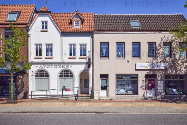 Residential and commercial buildings, row of houses, general architecture, historic pharmacy, tailoring, façade with windows, entrance with stairs and door, roofs, dormers, sidewalk, trees with spring leaves, blue sky, cloudless, street main street, leak, district of North Frisia, Schleswig-Holstein, Germany