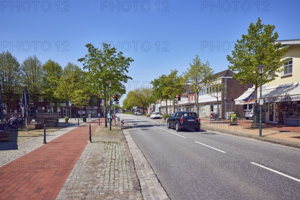 Residential and commercial buildings, general architecture, shops, retail, shopping, sidewalk, bricks, paving stones, street, central strip, vehicles, trees with spring leaves, blue sky, cloudless, main street, barrier bollard, leak, district of North Frisia, Schleswig-Holstein, Germany