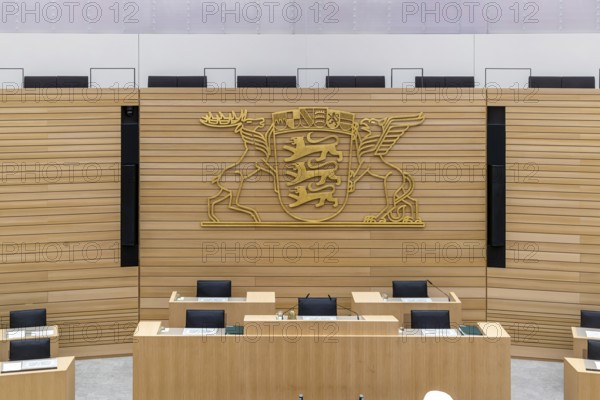 Plenary hall deserted with the seats of deputies and the government bank. Behind it is the coat of arms of the federal state. The state parliament of Baden-Württemberg is the state parliament based in Stuttgart, Baden-Württemberg, Germany