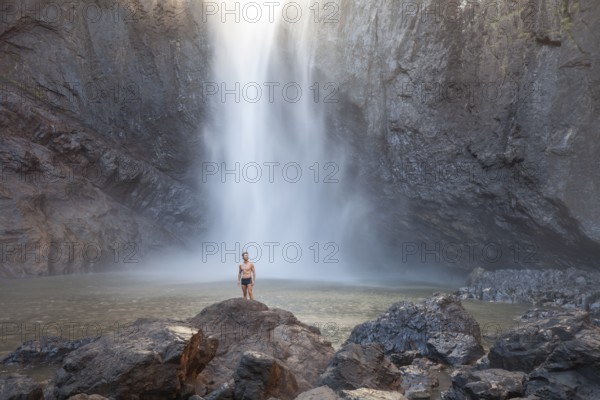 Daytime scene at Wallaman Falls with a fit man in swim trunks below the water fall, Queensland, Australia