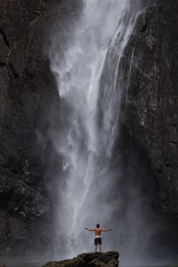 Daytime scene at Wallaman Falls with a fit man in swim trunks below the waterfall, Queensland, Australia