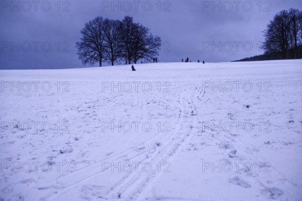 Snow-covered hill with people riding sledges under grey sky, Siegen