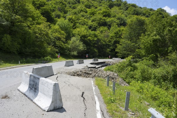 A damaged road with concrete barriers surrounded by dense green forest, road near Naduknari, Kakheti region, Georgia
