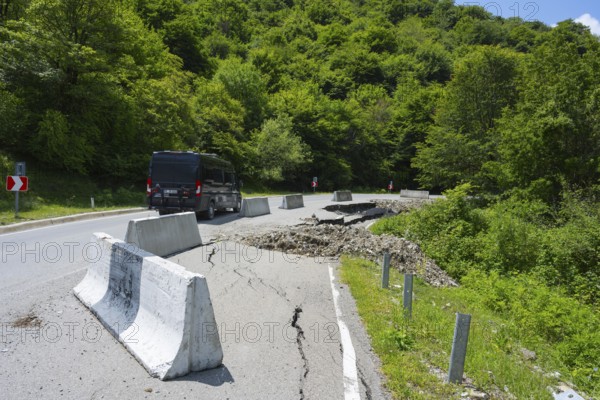 A black van drives on a damaged mountain road with concrete barriers, camper drives on road near Naduknari, Kakheti region, Georgia