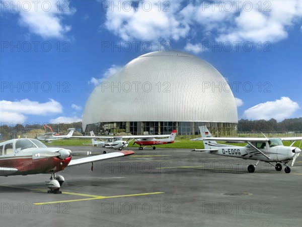 View of flight apron of Essen Mülheim airport with small aircraft parked at the front in the middle of the picture large Zeppelin Hall, Mülheim an der Ruhr, North Rhine-Westphalia, Germany