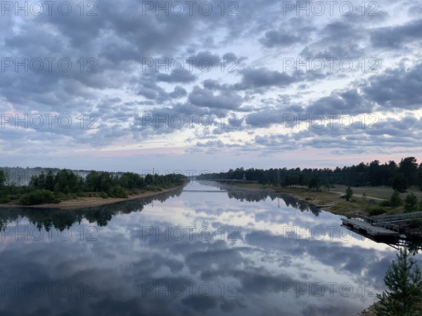 Tranquil river reflects dramatic sky and clouds amid wooded landscape, Vuotso, Lapland, Finland
