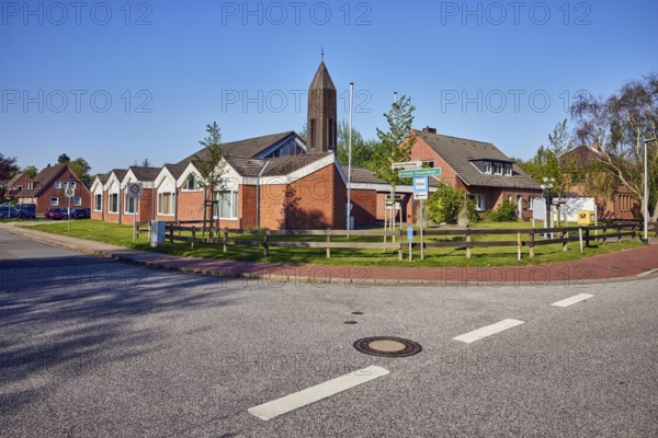 St. Ulrich Catholic Church, church tower, residential buildings, semi-detached houses, building material clinker, wooden fence, lawn, trees, blue sky, cloudless, intersection of Badallee with Deichgrafenweg, Sankt Peter-Ording, Nordfriesland district, Schleswig-Holstein, Germany