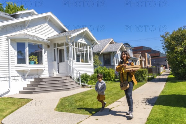 Mother and son carrying packages walking on a sidewalk in a residential neighborhood in calgary, alberta, enjoying the sunny summer weather and the beautiful houses
