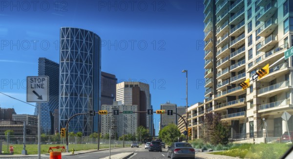 Cars driving on a multi lane road with the bow skyscraper and other modern buildings along the sides on a beautiful summer day in calgary, canada