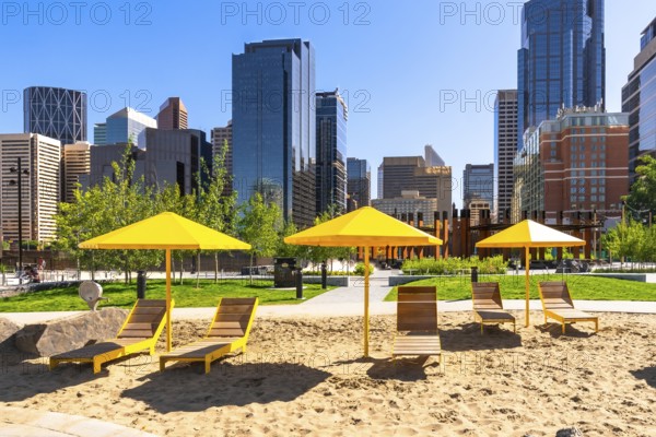 Yellow sun umbrellas and beach chairs create a vibrant pop of color against the backdrop of calgary's modern skyline, offering a unique urban beach experience
